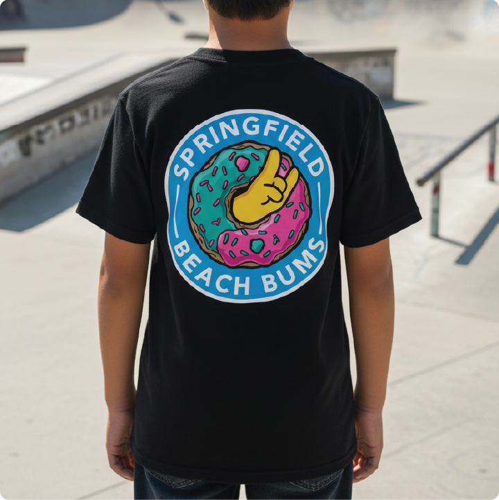 Child viewed from behind wearing a black T-shirt with a large colorful donut with pink and teal frosting, a yellow fist bump in the center, and the words “SPRINGFIELD BEACH BUMS” in white around the circle.