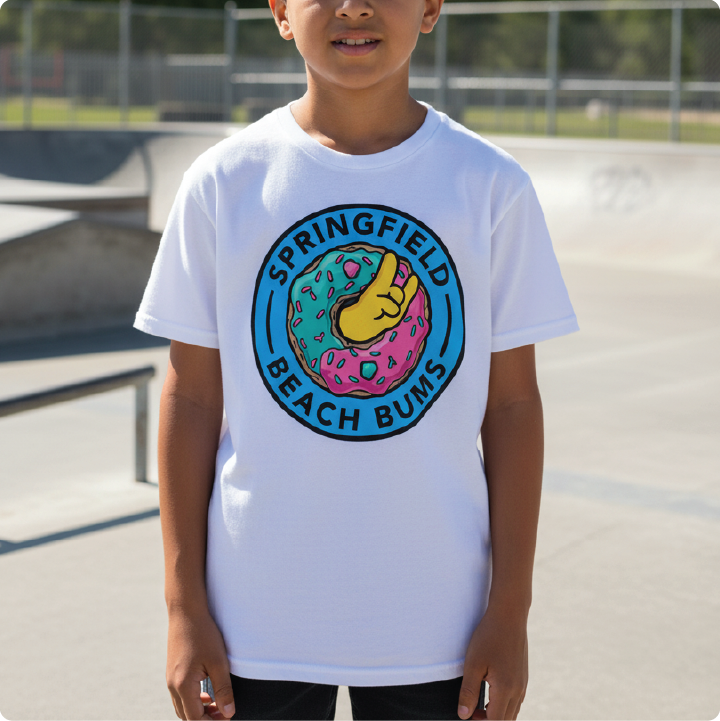 A child wearing a white short-sleeve t-shirt with a colorful circular graphic on the chest that reads 'SPRINGFIELD BEACH BUMS' around a donut illustration, photographed outdoors at a skatepark.