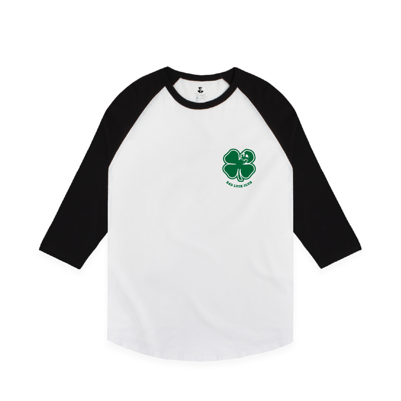 Front view of a black and white raglan t-shirt with a small green clover design on the chest area with green 'Bad Luck Club' text.