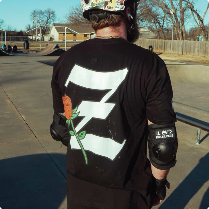 Person wearing a black t-shirt with a white Z logo and red rose, standing in a skate park.