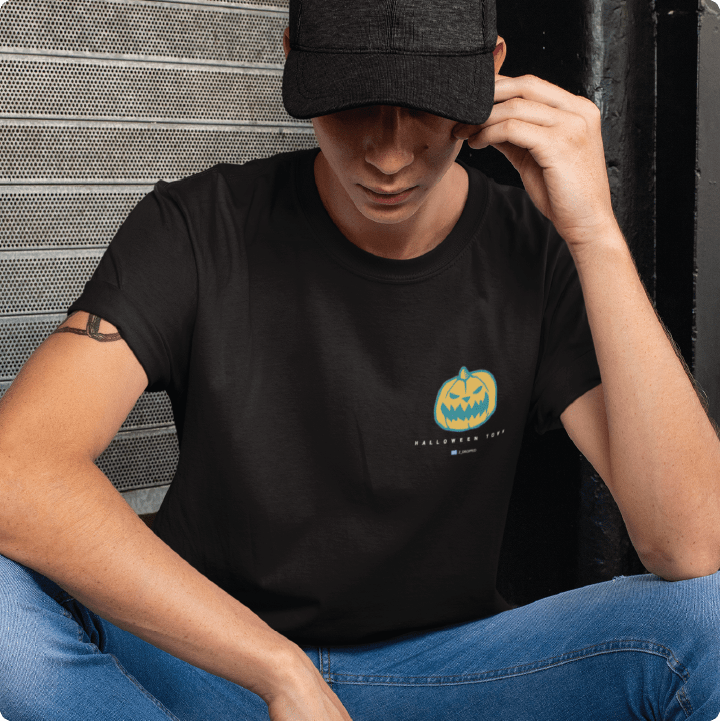 Person wearing a black t-shirt with a pumpkin design and text, sitting against a metallic wall.