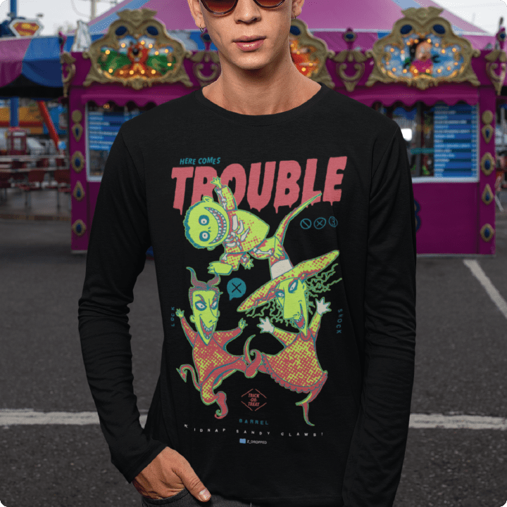 Person wearing a black long-sleeve shirt with colorful graphic design and 'TROUBLE' text at an amusement park.