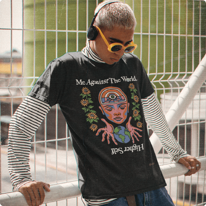 Person wearing a black graphic t-shirt with colorful design and text, standing against a metal fence.