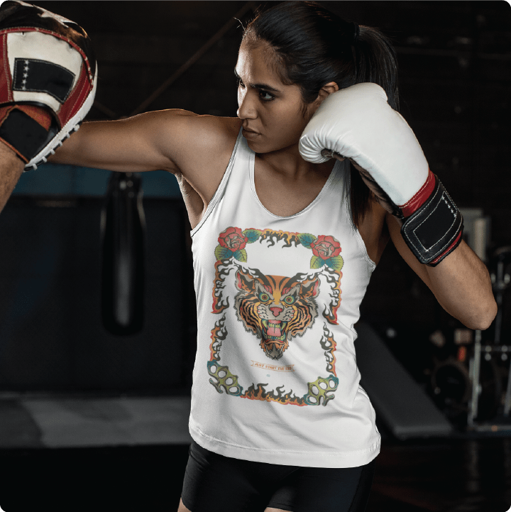 Person wearing a white tank top with a tiger design and boxing gloves in a gym setting.