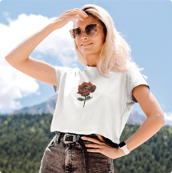 Person wearing a white t-shirt with a rose graphic outdoors against a mountainous background
