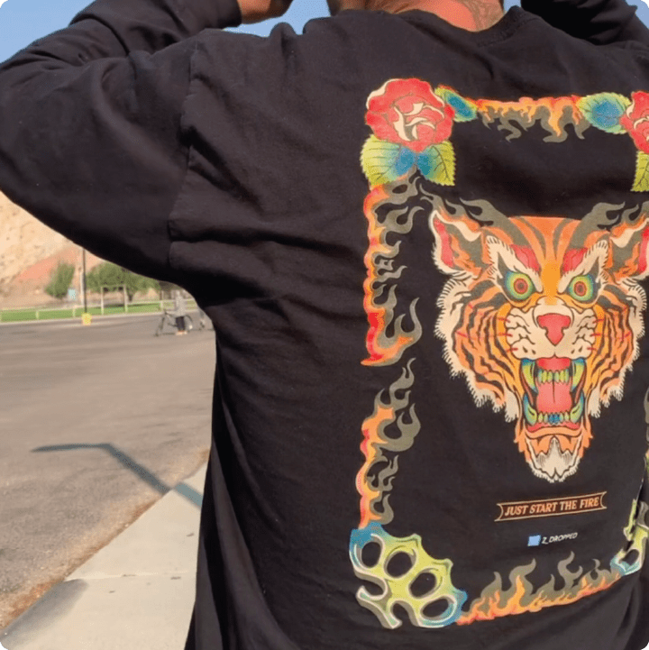 Person wearing a black long-sleeve shirt with a colorful tiger design on the back at a skate park.