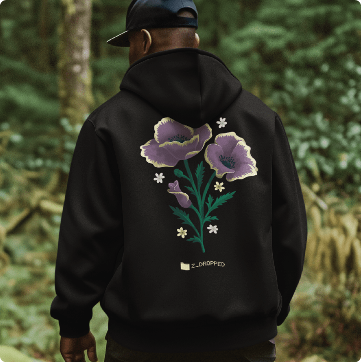 Rear view of a man wearing a unisex black hoodie with purple poppy floral design walking through the forest.