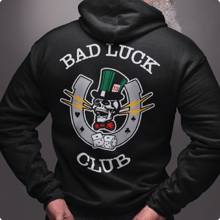 Rear view of a unisex black hoodie with 'Bad Luck Club' design featuring a high roller skull head with a green top hat with the number 13 and red bowtie  inside a grey horseshoe with rolling dice.