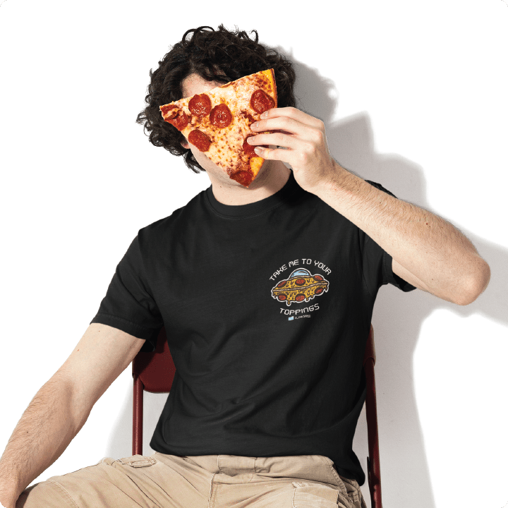 Young man wearing a black pizzabduction t-shirt covering his face with a slice of pizza sitting in a chair against a a white wall. 