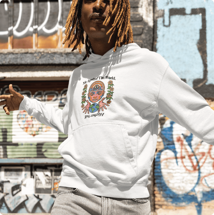 Young man wearting a unisex white hoodie with black 'Me Against The World Higher Self' text in an urban setting.