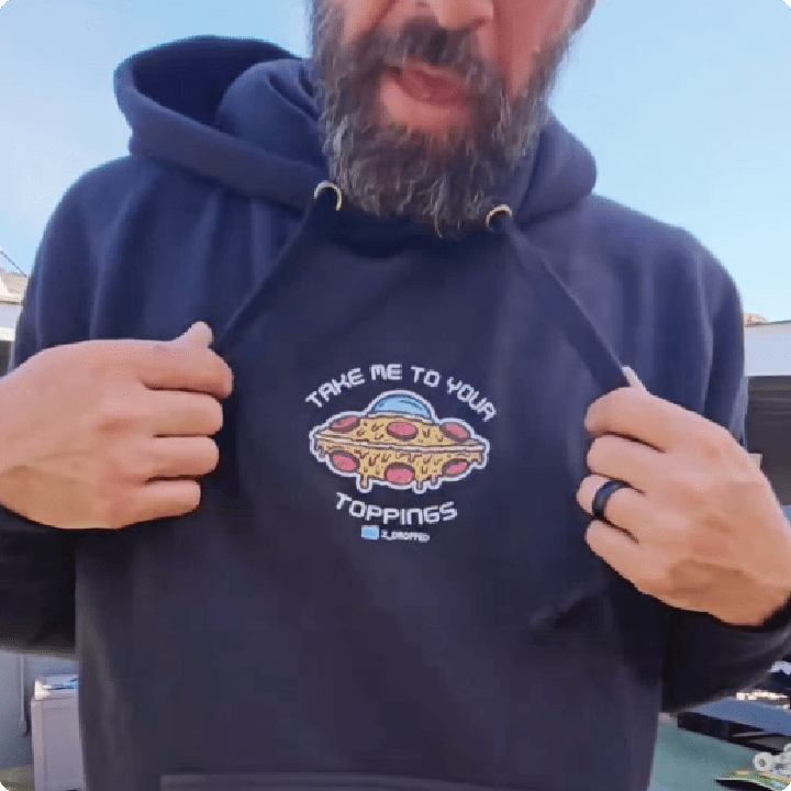 Person wearing a black hoodie with a pizza-ufo-themed graphic and 'Take me to your toppings' white text.