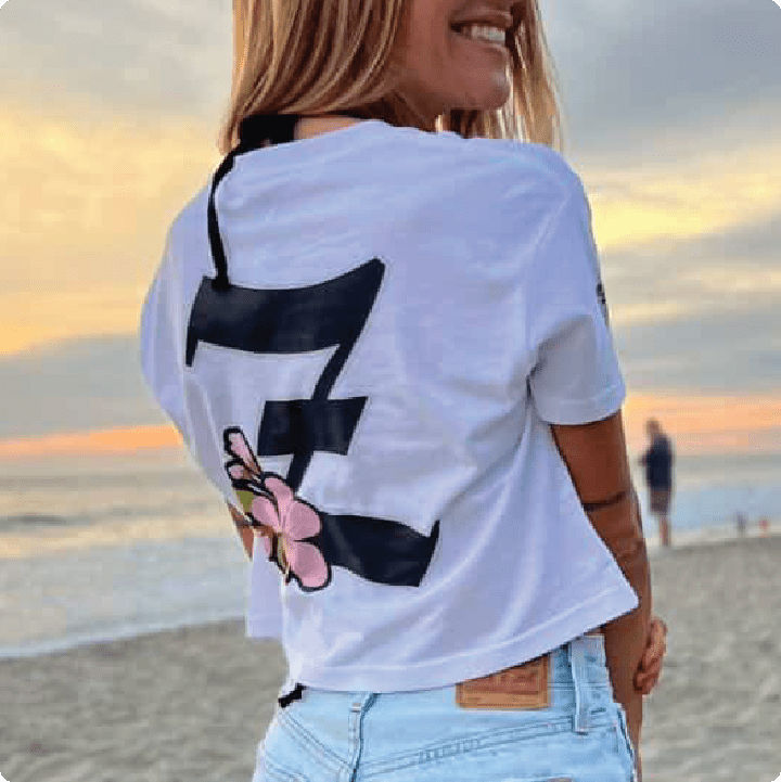 Woman wearing a white t-shirt with black and pink design on a beach at sunset