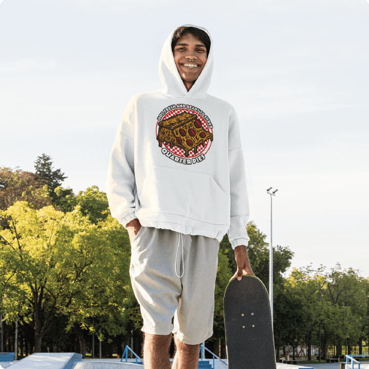 Person wearing a unisex white zdropped quarter pie hooded sweatshirt holding a skateboard at a skate park. 