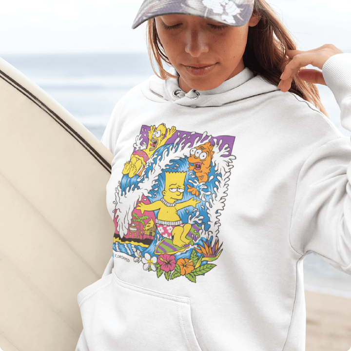Person holding a surfboard wearing a unisex white hoodie with Bart and Homer Simpson surfing a wave standing on the beach.