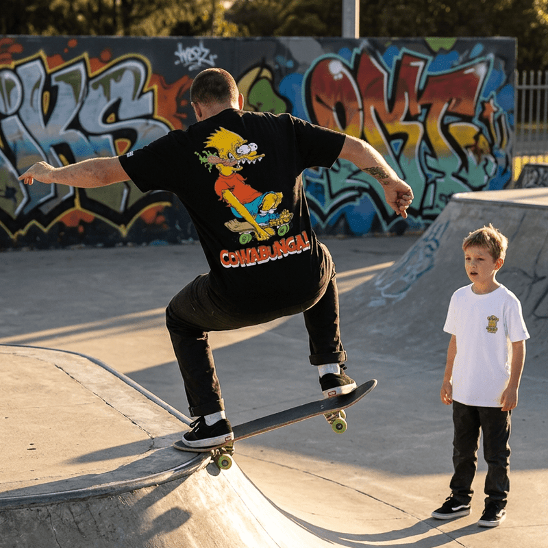 Older man doing a skate trick at a skate park with his kid wearing a black Bart Roth T-shirt