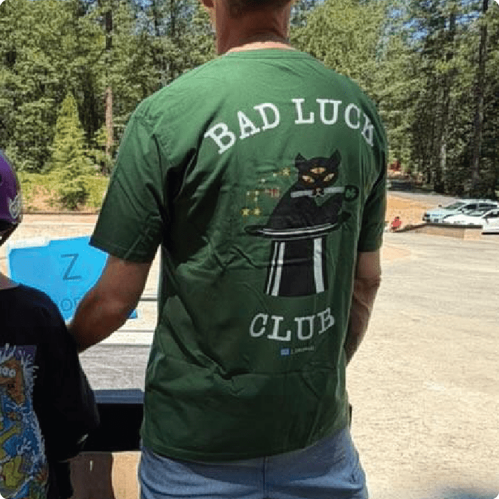 Raer view of a person wearing a green t-shirt with 'Bad Luck Club' design outdoors.