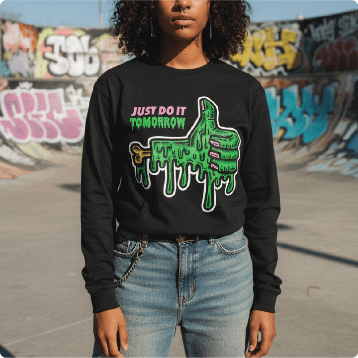 Person wearing a black long sleeve shirt with a slimy thumbs up graphic and text, standing in front of graffiti art.