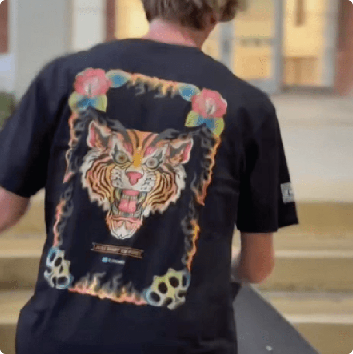very blurry picture of a rear view black t-shirt on jeff dechesare wearing a flaming tiger graphic holding a skateboard.