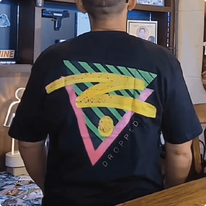 Person wearing a black t-shirt with colorful geometric design on the back, sitting indoors.
