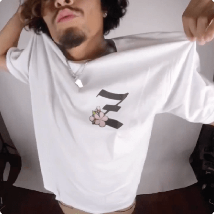 Person holding a white t-shirt with a black Z and cherry blossom design in a studio.