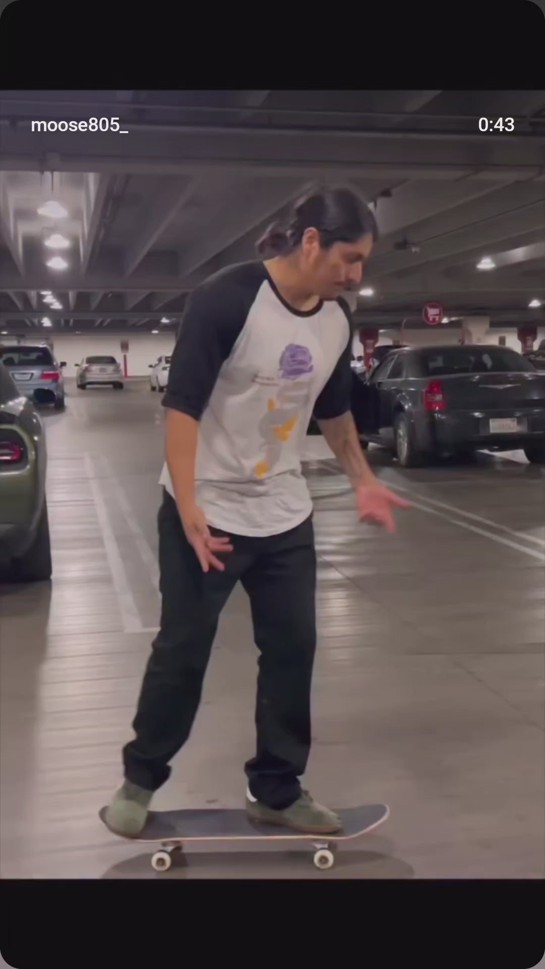 Moose wearing a mamba quote three quarter sleeve raglan doing skateboard tricks in a parking lot