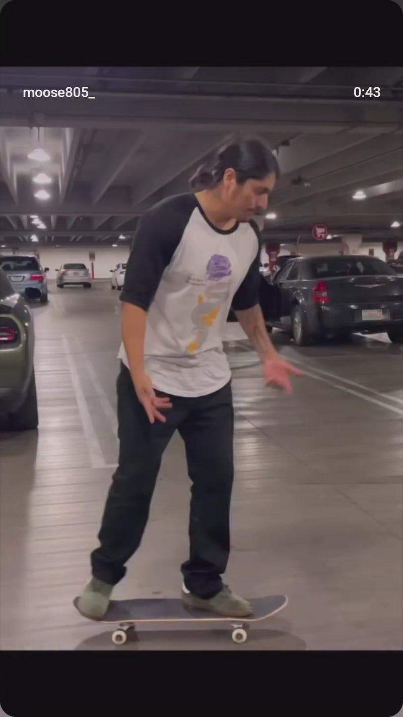 Moose wearing a mamba quote three quarter sleeve raglan doing skateboard tricks in a parking lot