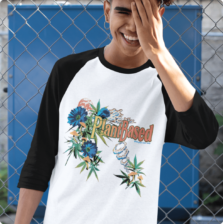 Person wearing a white and black baseball shirt with 'PlantBased' design in front of a chain-link fence.