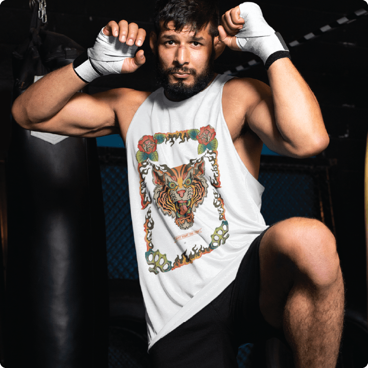 Person wearing a white tank top with a colorful tiger design, sitting in a boxing ring.