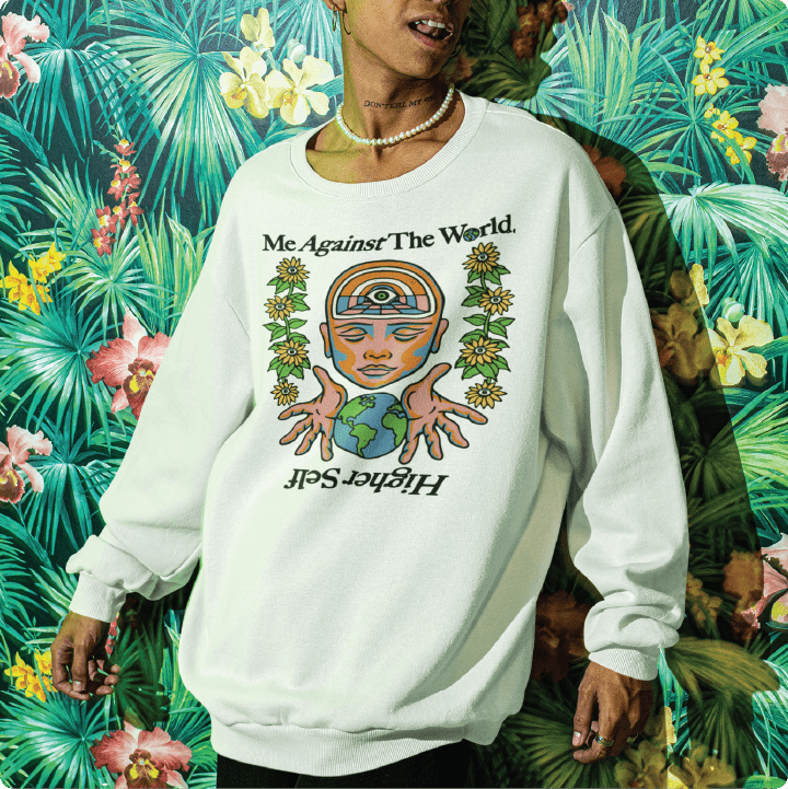 Person wearing a white long sleeve t with a graphic on the front leaning against a tropical background