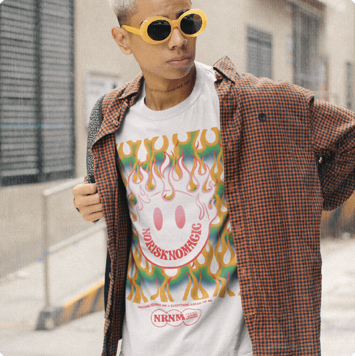 Person wearing a colorful t-shirt with a flaming smiley face design and plaid button down outdoors.