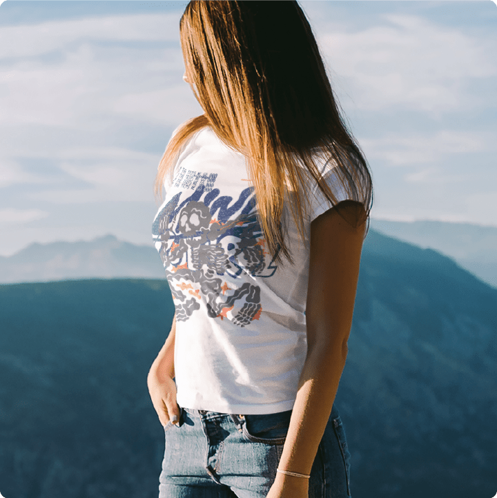 Person wearing a white t-shirt with colorful graphics standing against a mountainous landscape.