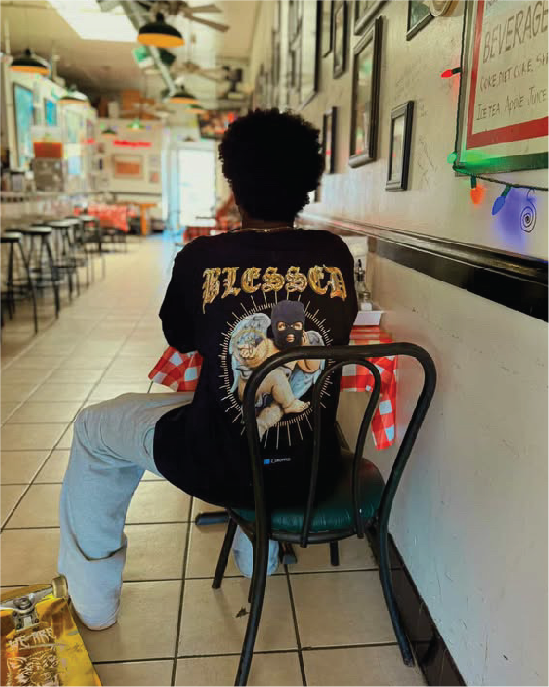 Person sitting at a diner table wearing a black'BLESSED' long sleeve tee with a cherib graphic.