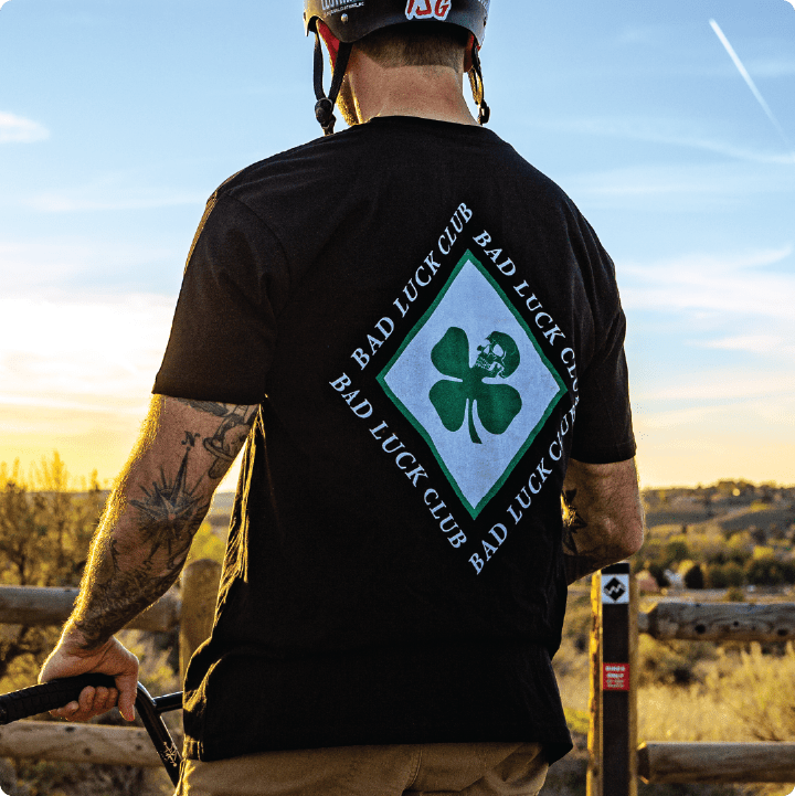 Person wearing a black 'Bad Luck Club' t-shirt with a shamrock design, standing outdoors.