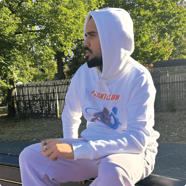 RpmieTheKid wearing a white zdropped not of this earth hoodie sitting outdoors.
