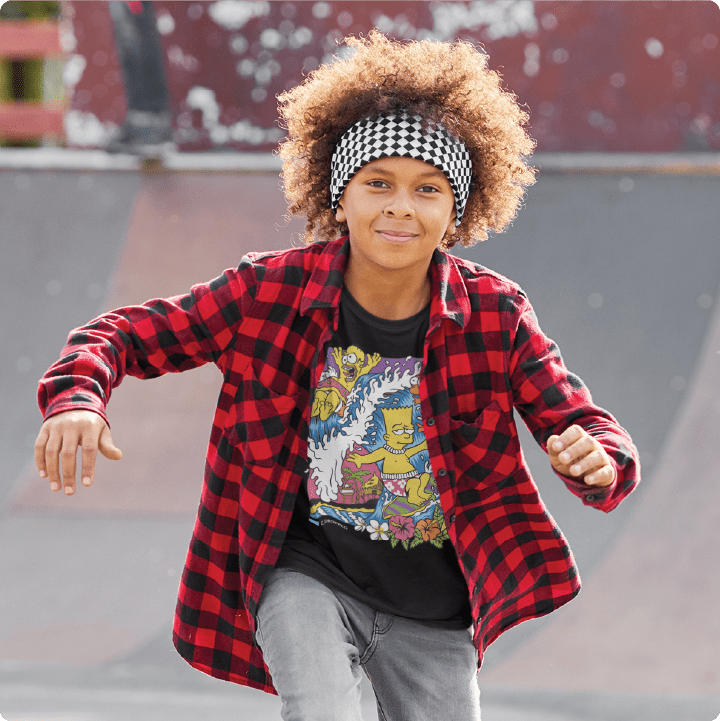 Child wearing a red plaid shirt over a black bartsunami zdropped graphic t-shirt with a checkered headband, skating in a skate park.