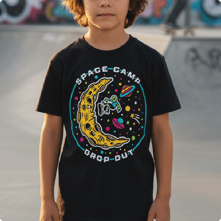 Child wearing a black t-shirt with a colorful 'Space Camp Drop Out' design at a skate park.